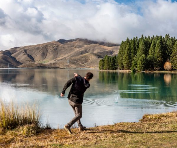 Un homme vêtu d'un pull et d'un pantalon noirs jette des cailloux dans un lac