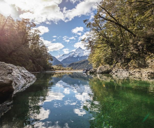 Ruisseau ensoleillé, arbres verts et sommets enneigés au loin